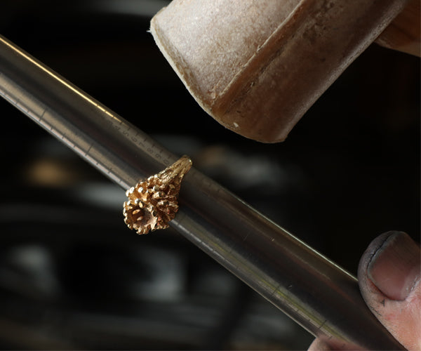 Un bijoutier ajuste la taille d’une bague en or à l’état brut à l’aide d’un triboulet gradué et d’un maillet en cuir, étape essentielle avant le polissage et la finition.