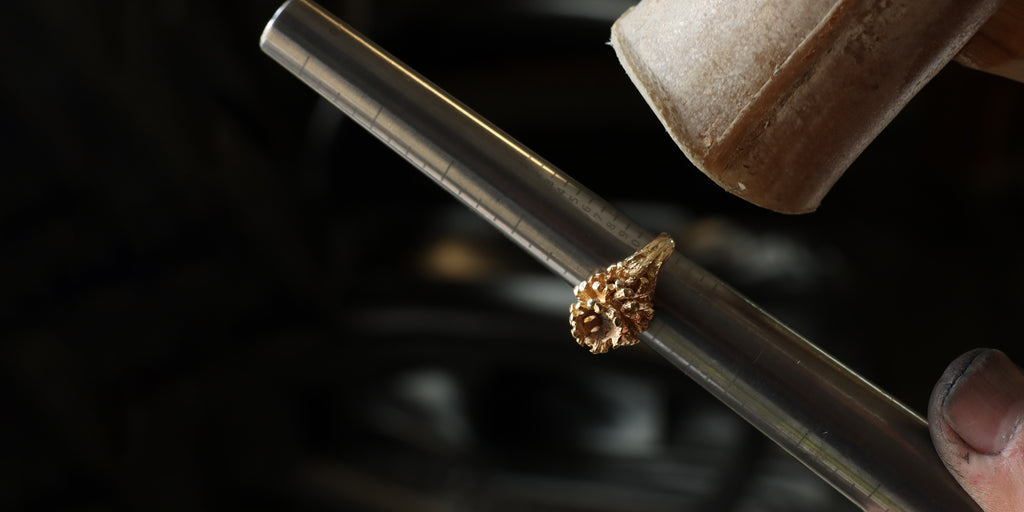 Un bijoutier ajuste la taille d’une bague en or à l’état brut à l’aide d’un triboulet gradué et d’un maillet en cuir, étape essentielle avant le polissage et la finition.