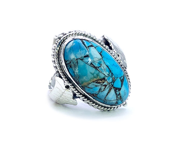 Bague ancienne en or blanc restaurée, ornée d’une grande turquoise ovale à inclusions naturelles, mise en valeur par un serti détaillé de style vintage avec motif de corde torsadée et feuilles sculptées à la main.