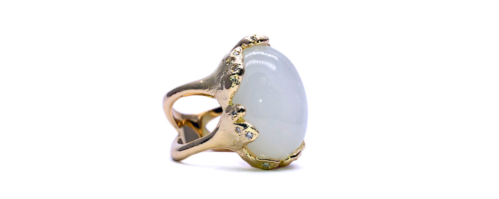 Bague restaurée en or jaune au design organique et sculptural, sertie d’une pierre de lune blanche en cabochon et rehaussée de petits diamants. Une pièce à l’allure extravagante qui allie mystère et élégance.