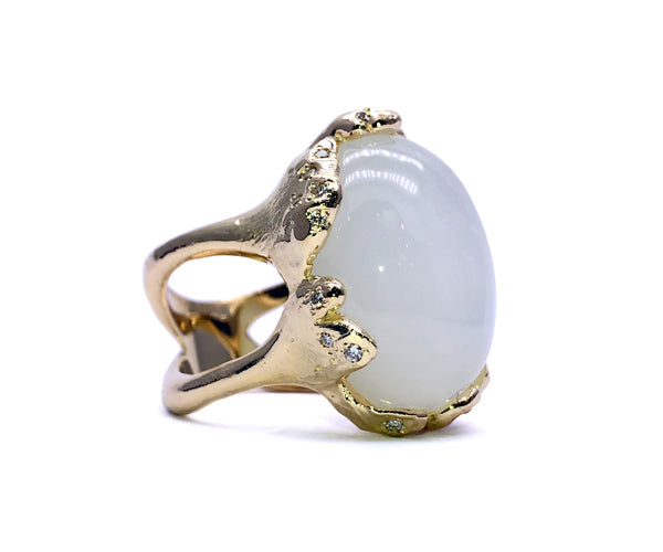 Bague restaurée en or jaune au design organique et sculptural, sertie d’une pierre de lune blanche en cabochon et rehaussée de petits diamants. Une pièce à l’allure extravagante qui allie mystère et élégance.