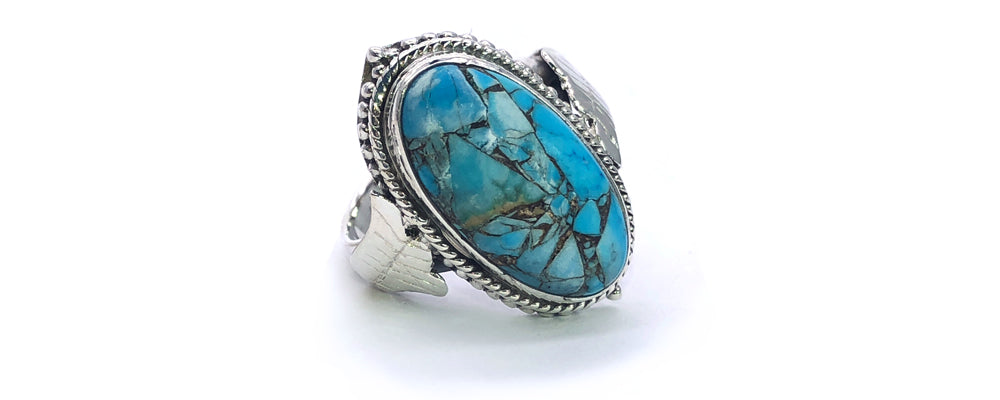 Bague ancienne en or blanc restaurée, ornée d’une grande turquoise ovale à inclusions naturelles, mise en valeur par un serti détaillé de style vintage avec motif de corde torsadée et feuilles sculptées à la main.