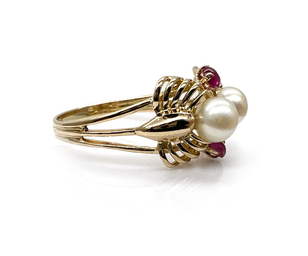 Bague restaurée en or jaune, composée de deux perles blanches encadrées de petits rubis. Le corps de bague à double anneau est maintenu par une structure ajourée en forme de panier, typique des designs vintage.