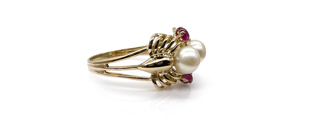 Bague restaurée en or jaune, composée de deux perles blanches encadrées de petits rubis. Le corps de bague à double anneau est maintenu par une structure ajourée en forme de panier, typique des designs vintage.