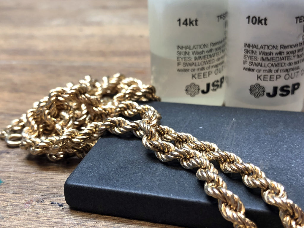 Chaîne en or posée sur une plaque de test avec flacons JSP pour l’analyse du carat.