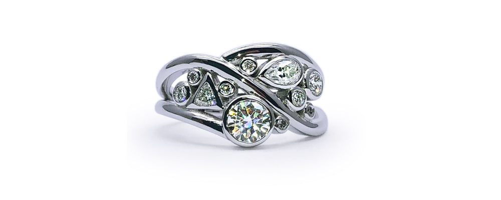 Création sur mesure en or blanc au design organique et enveloppant. Le corps de bague aux lignes croisées crée un mouvement fluide, mettant en valeur un mélange de diamants de formes variées — ronde, poire et triangle — en sertis clos.