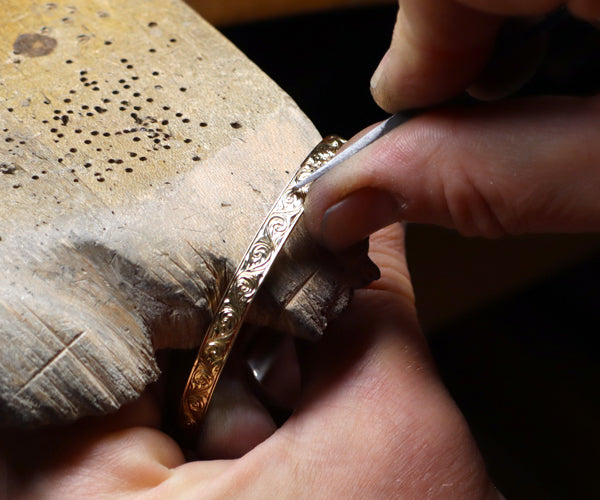 Montage photo présentant une bague en or jaune gravée de motifs floraux avec diamants et un bracelet en cours de gravure manuelle par une artisane joaillière chez Flamme en rose.