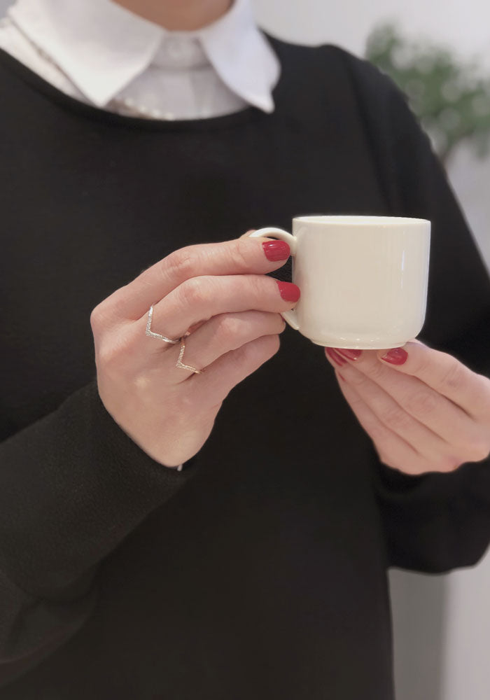 Une joaillière de Montréal tenant une tasse à café avec des bagues en or et diamants dans sa main droite